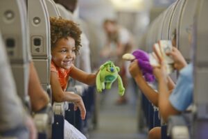 Uma Criança falando com outra no corredor de um avião enquanto mostra o seu brinquedo verde, a outra mostra seu brinquedo azul