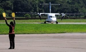 Avião ao fundo manobrando na pista de pouso, no primeiro plano um manobrista de avião fazendo sinal.