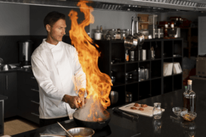 Cozinheiro fazendo prato com a panela lançando uma grande labareda